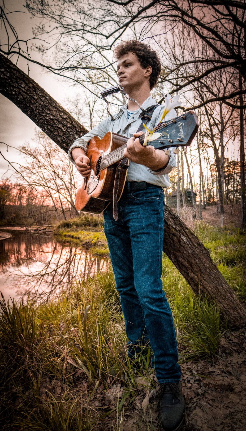 Musician playing acoustic guitar in natural outdoor setting with warm golden hour lighting