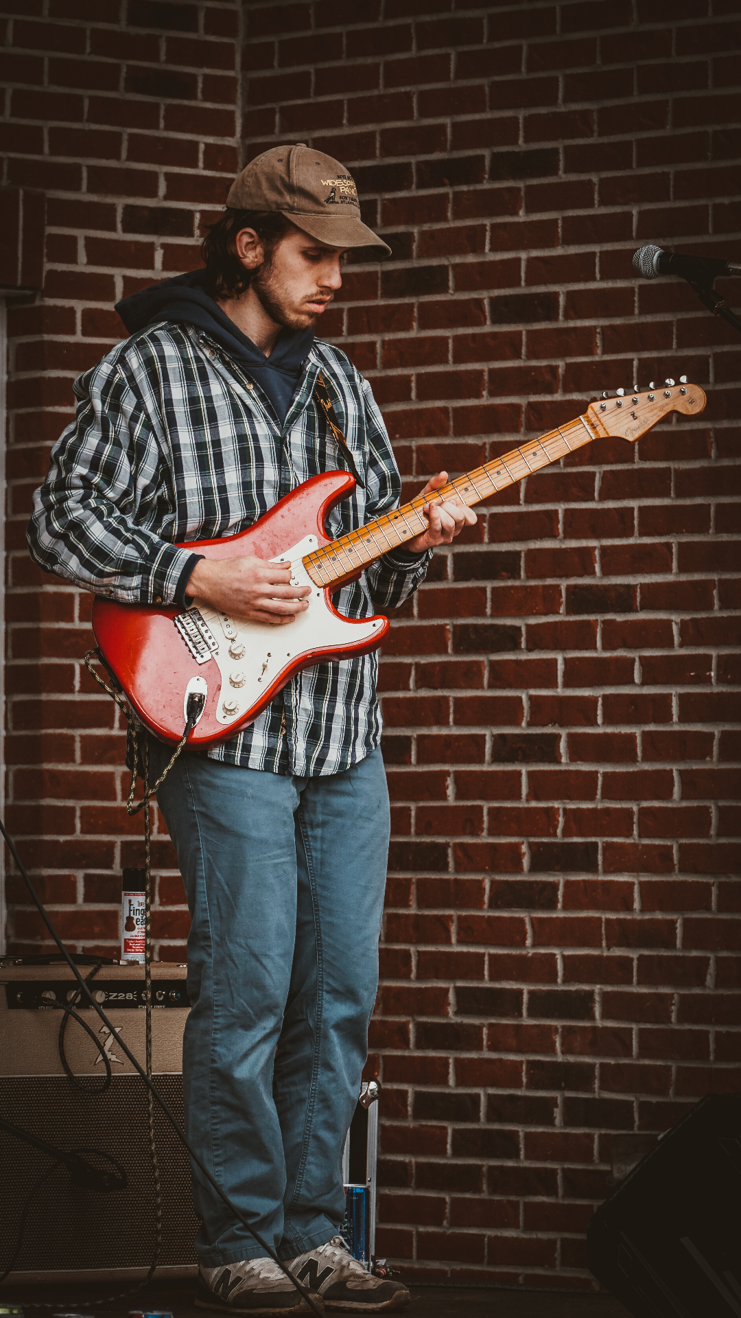 Solo electric guitarist performing with red Stratocaster against industrial brick wall backdrop