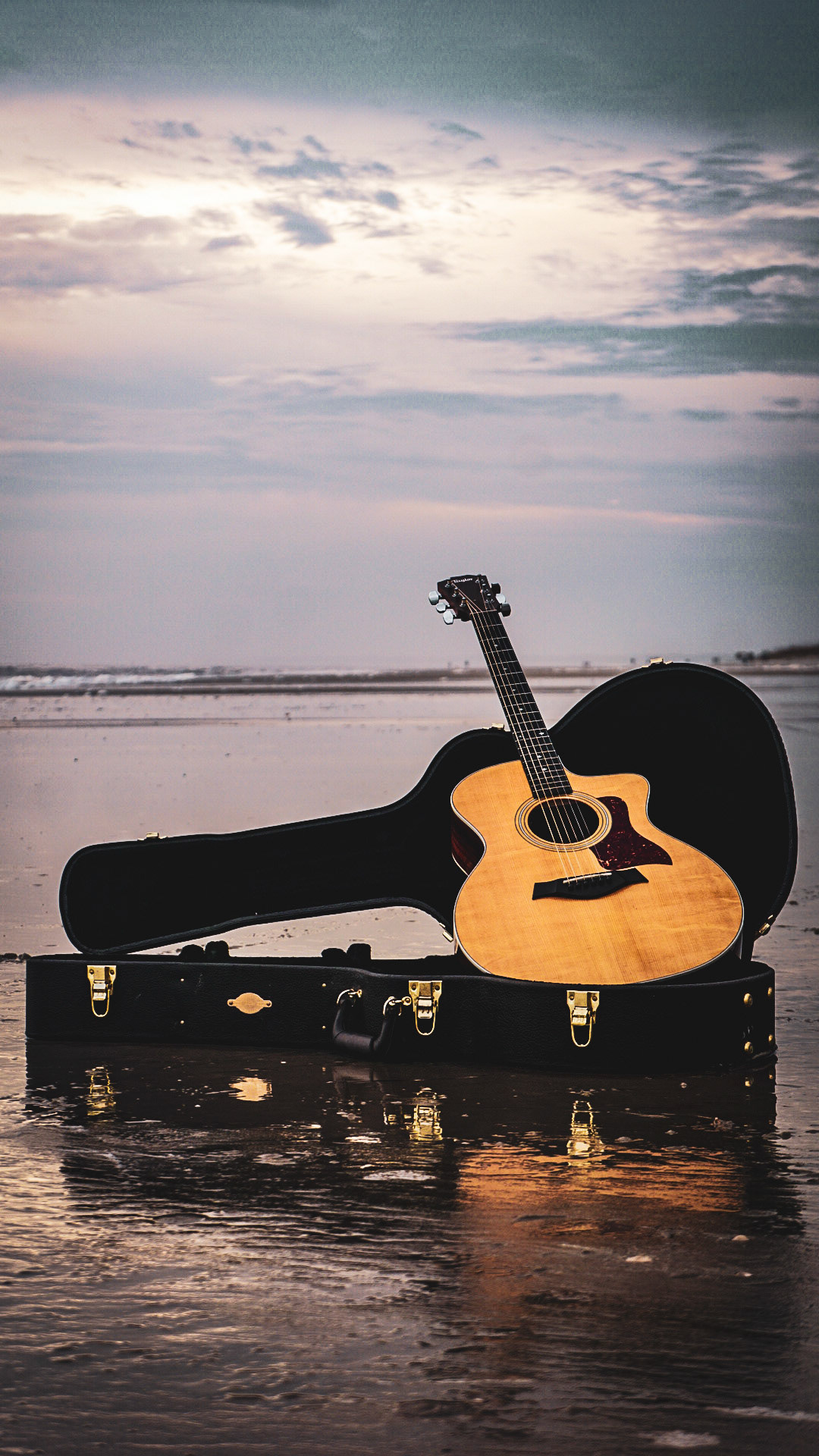 Acoustic guitar in open case on beach during golden hour sunset with dramatic sky