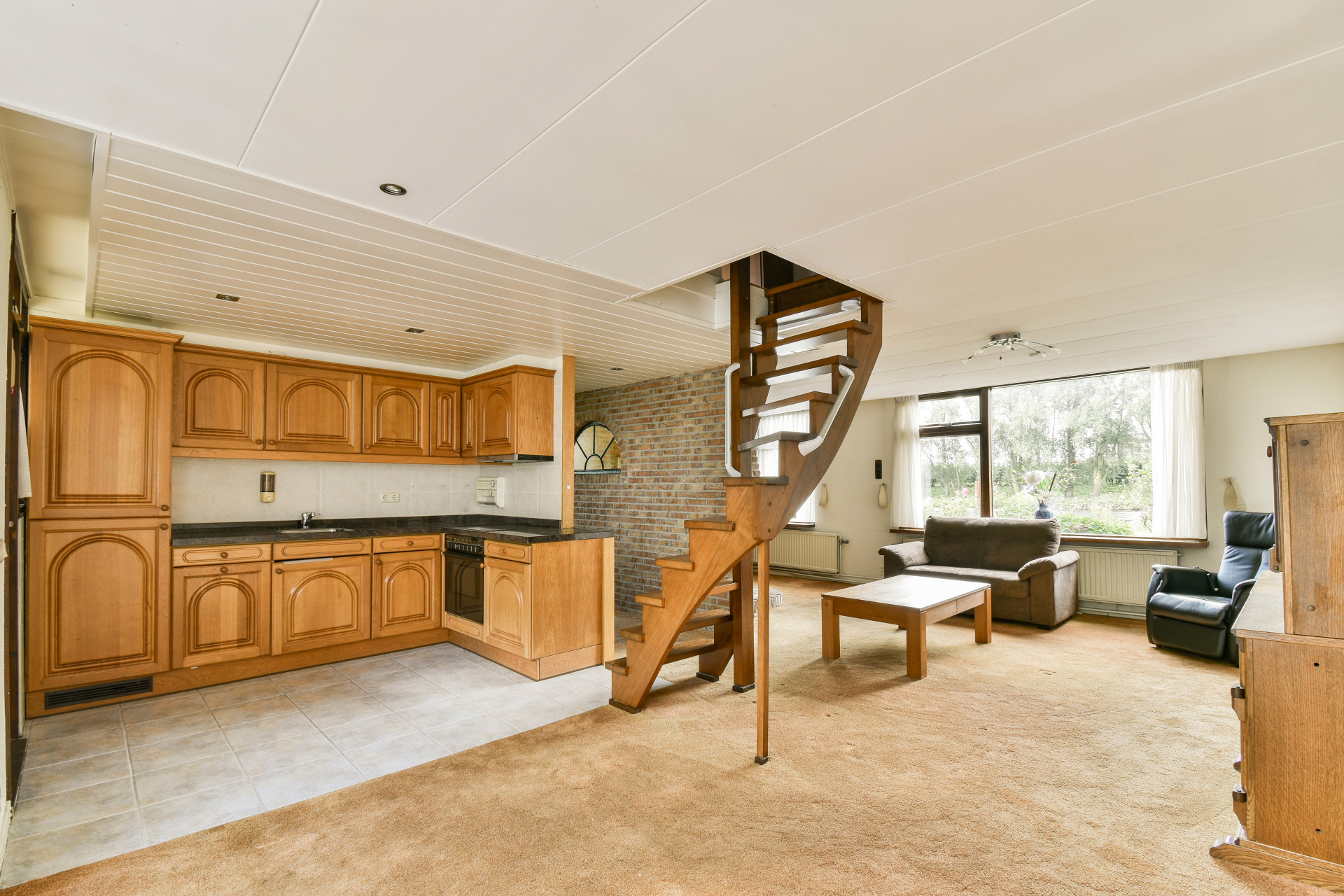 Open kitchen and living space with wooden spiral staircase and brick accent wall