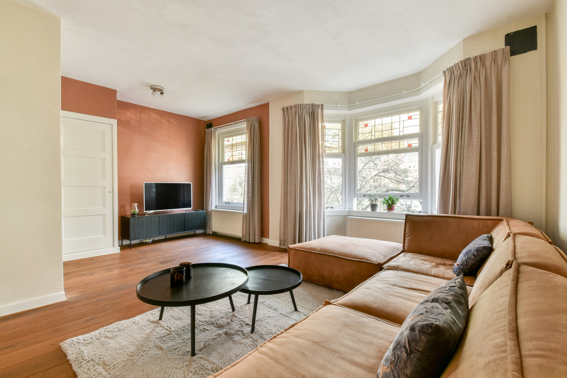 Comfortable living room with large bay windows and tan leather sectional sofa