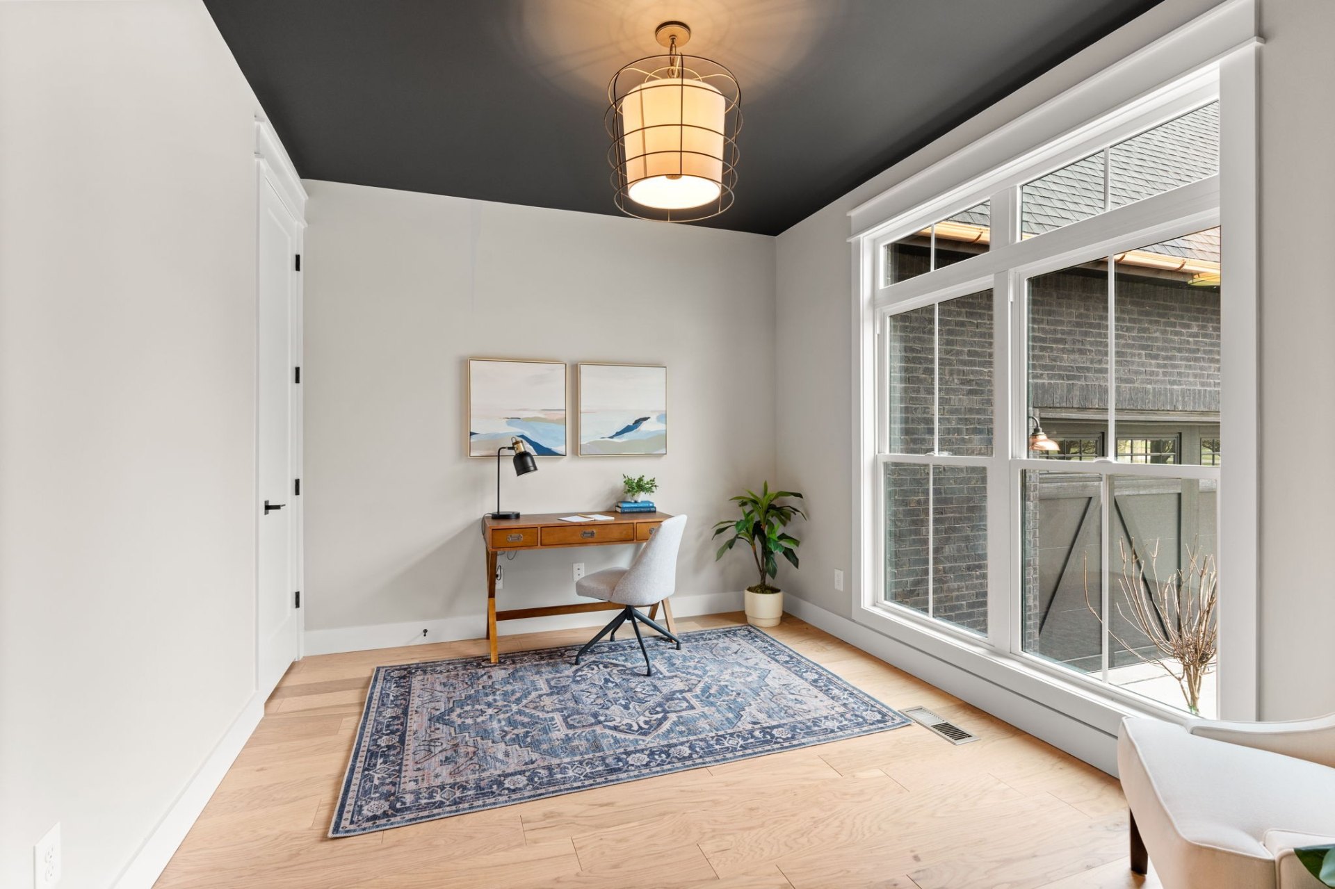 Elegant home office with dark painted ceiling, vintage desk and large garden windows