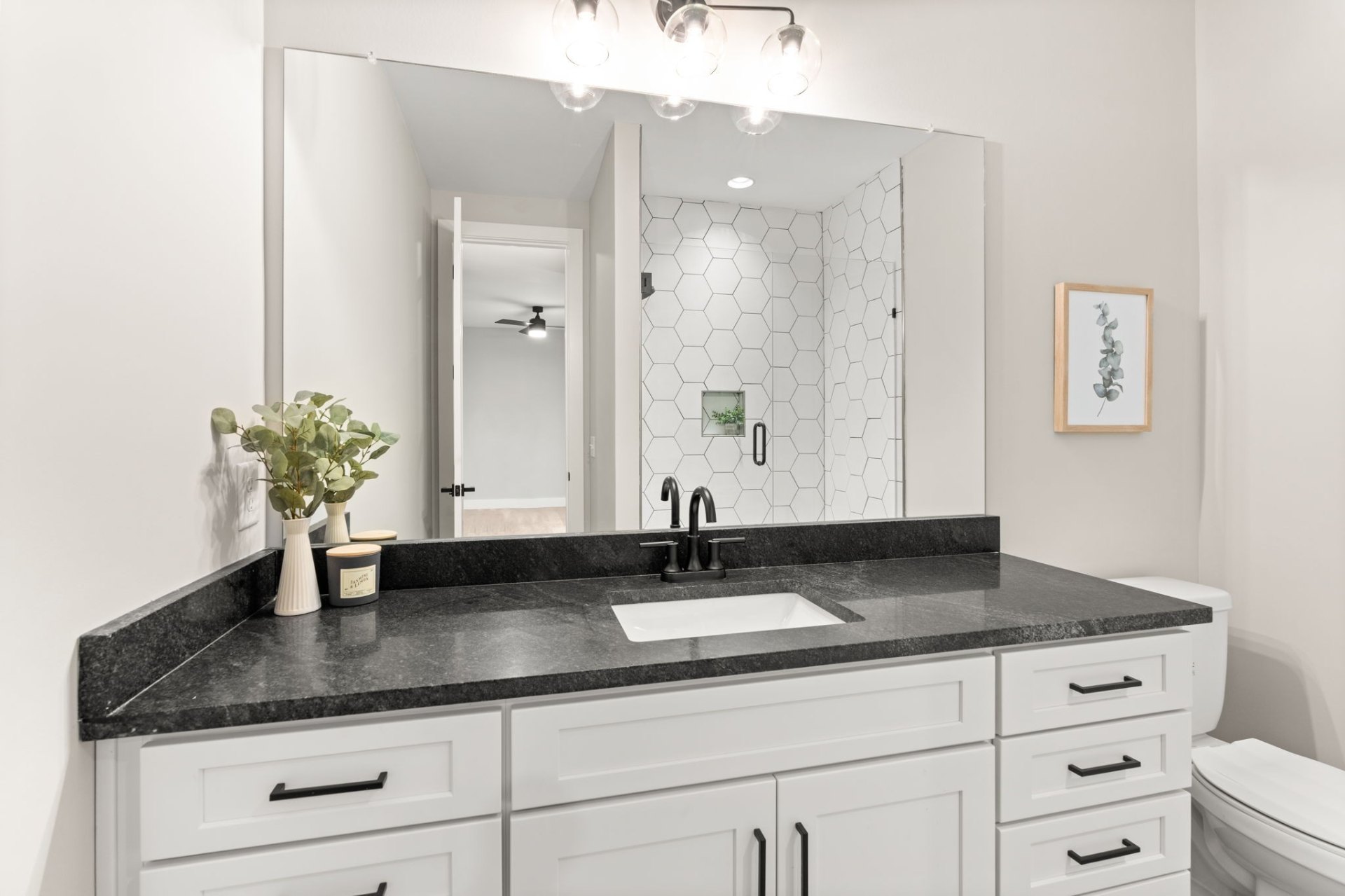 Luxurious bathroom with black granite countertops, white cabinetry and hexagonal shower tile