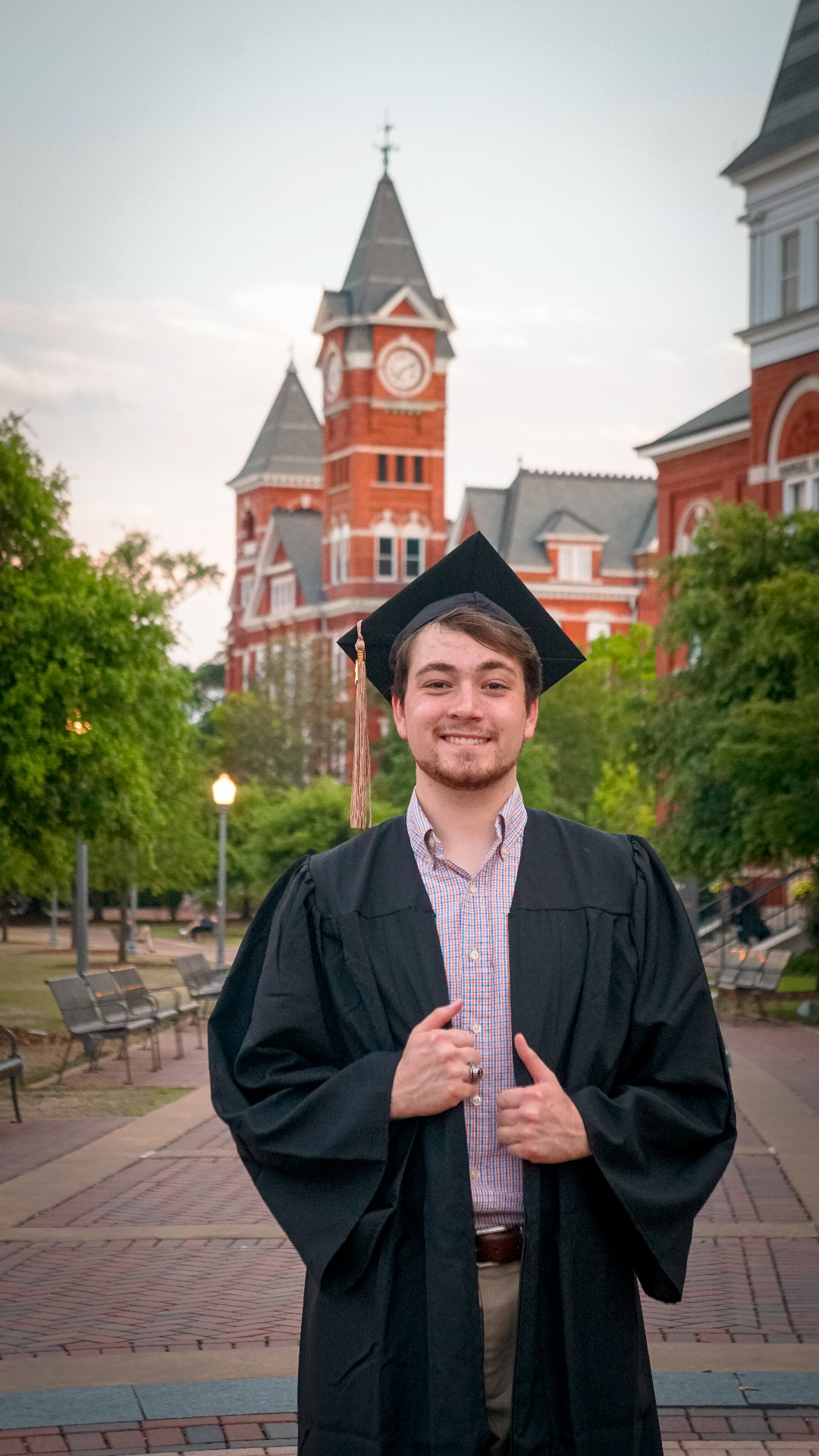 Graduate in cap and gown portrait on university campus with historic clock tower backdrop