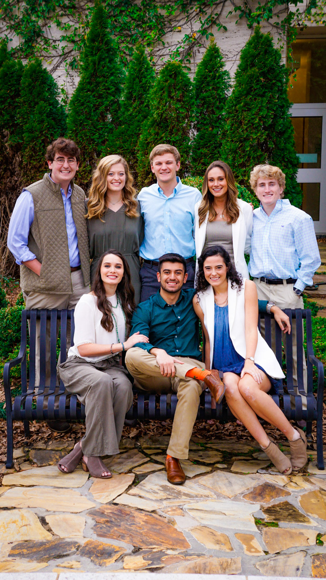 Professional group portrait of friends sitting on park bench with natural greenery backdrop