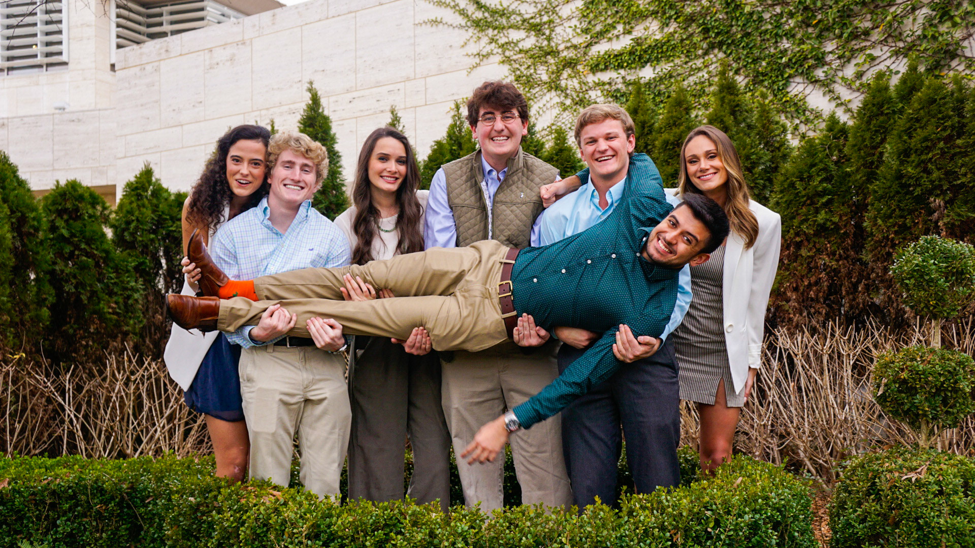 Fun group portrait of friends with one person being lifted up in outdoor garden setting