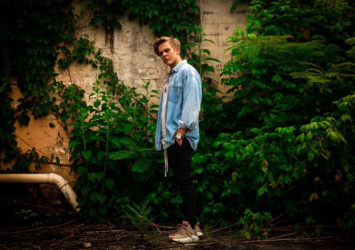 Artistic male portrait in natural outdoor setting with lush greenery and ivy backdrop