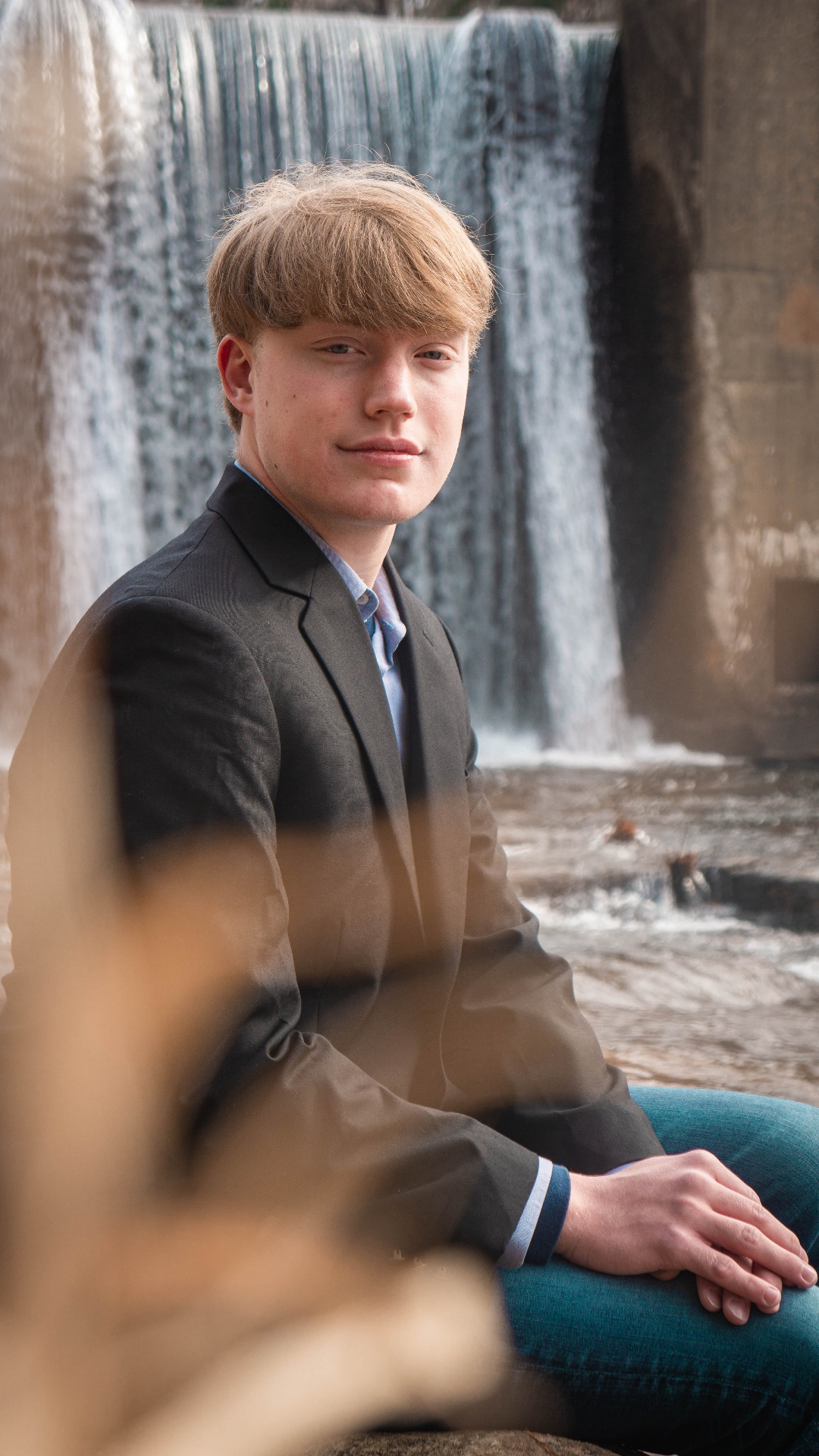 Professional formal portrait of young man in gray suit with dramatic waterfall backdrop