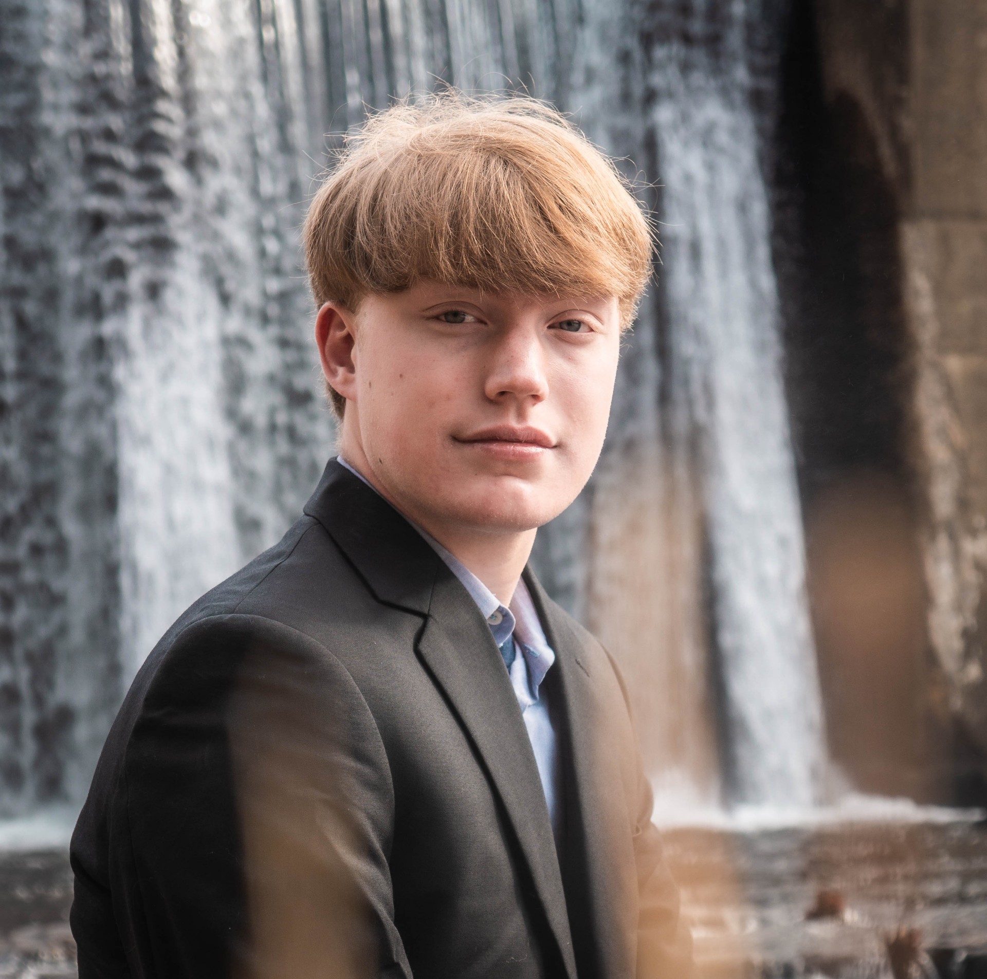 Professional portrait session with young man in formal attire by scenic waterfall